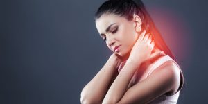 A lady holding her neck as she looks in pain. She is grasping her neck with two hands. The pain is highlighted with red on the area