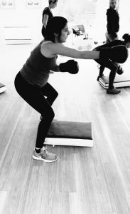 A pregnant lady having a work out. She is wearing boxing gloves and stands in a squat position. The photo is in black and white